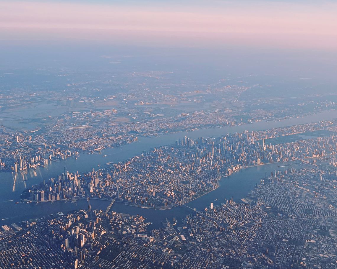 Aerial view from an airplane window of the sunrise light illuminating Brooklyn, Queens, Manhattan, and New Jersey.